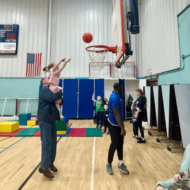 Grandpa holding up granddaughter to shoot basketball into hoop