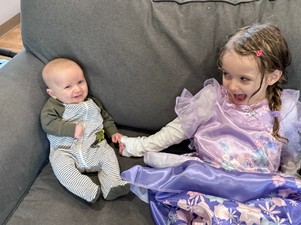 Sister holding baby brother's hand on couch