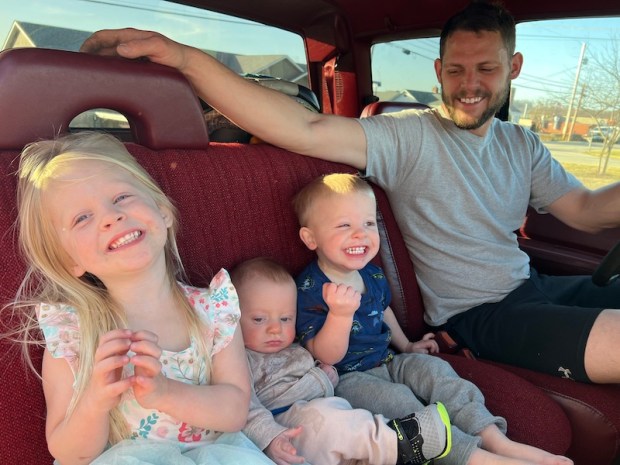 Three young kids sitting by dad in truck