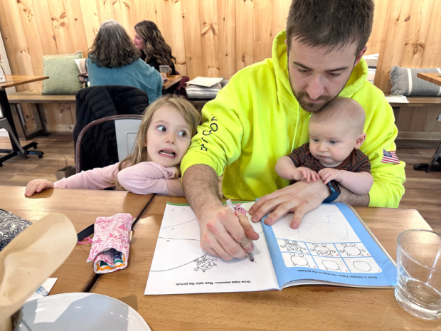 Dad doing school with four year old and baby at table in a tea shop