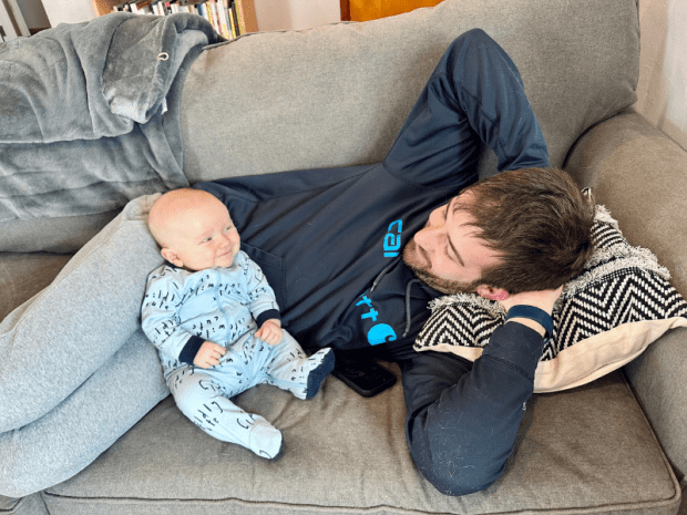 Dad and baby boy sitting on couch together smiling at each other