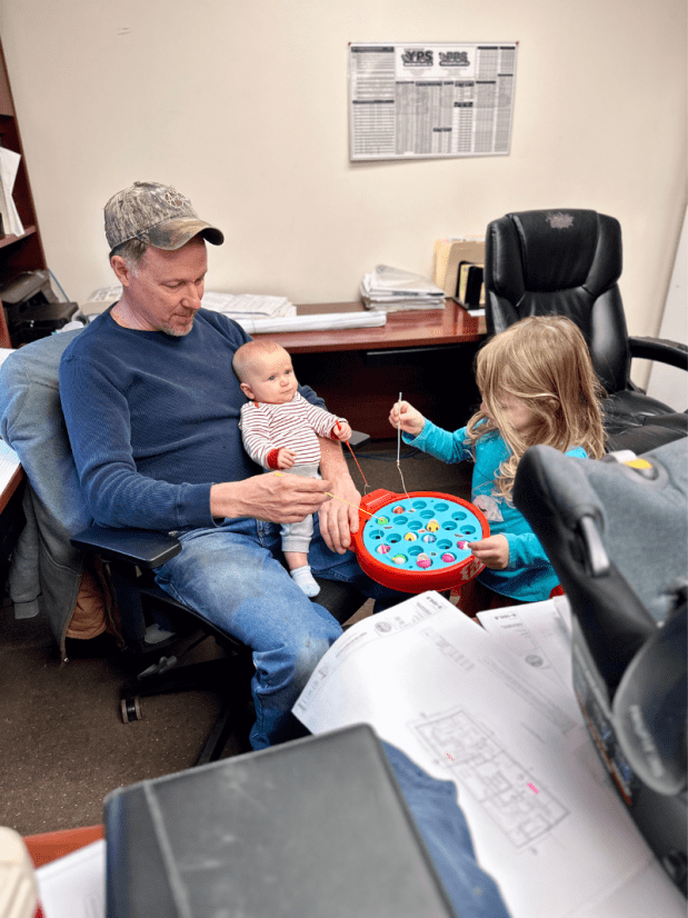 Girl playing fishing game with grandpa while he holds baby