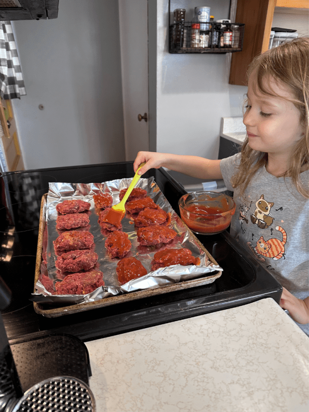 Girl brushing meatloaf with ketchup