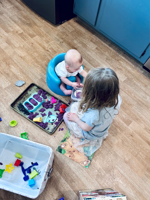 Girl and baby playing with kinetic sand on floor