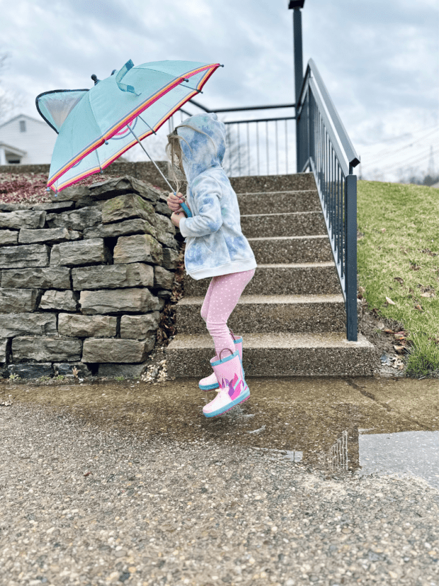Girl holding umbrella and jumping in puddle