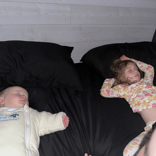 Baby and big sister sleeping in bed