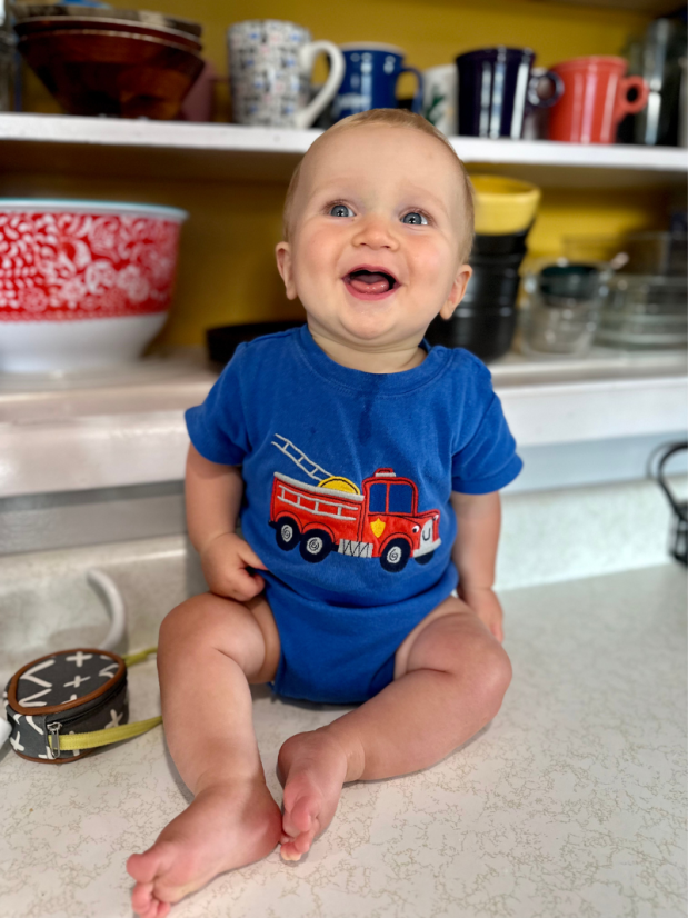 Baby boy wearing firetruck onesie sitting on kitchen counter
