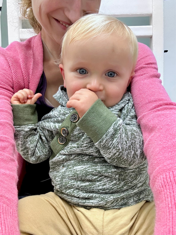 Baby boy smiling and sucking his thumb on mom's lap