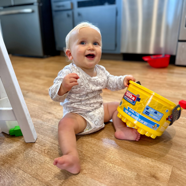 11 month old baby boy sitting on kitchen floor with bucket of blocks