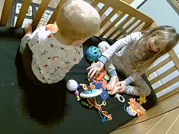 Older sister with baby brother in his crib with toys on baby monitor