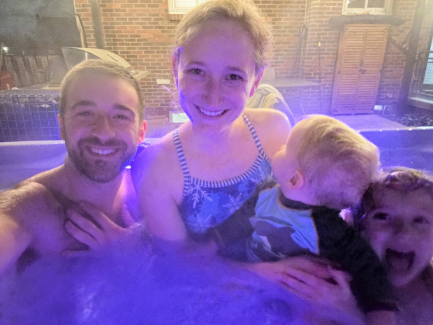 Family selfie with mom, dad, girl, and baby boy in hot tub at night