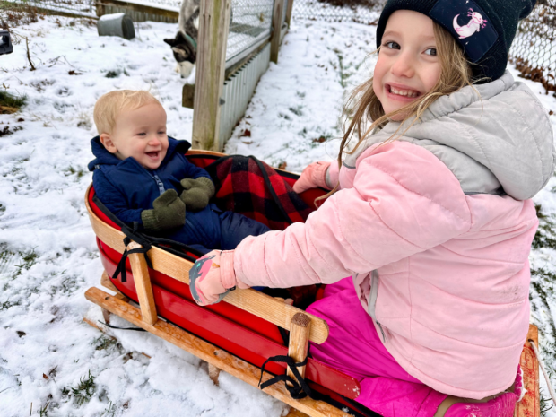 Big sister and baby brother sitting in sled together