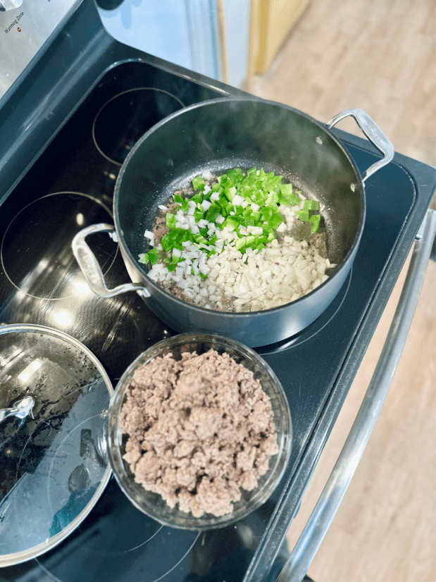 Green peppers and onions cooking on stove with ground beef next to it to make chili