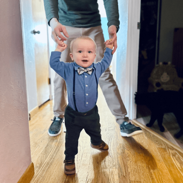 Baby boy standing and holding onto dad's hands