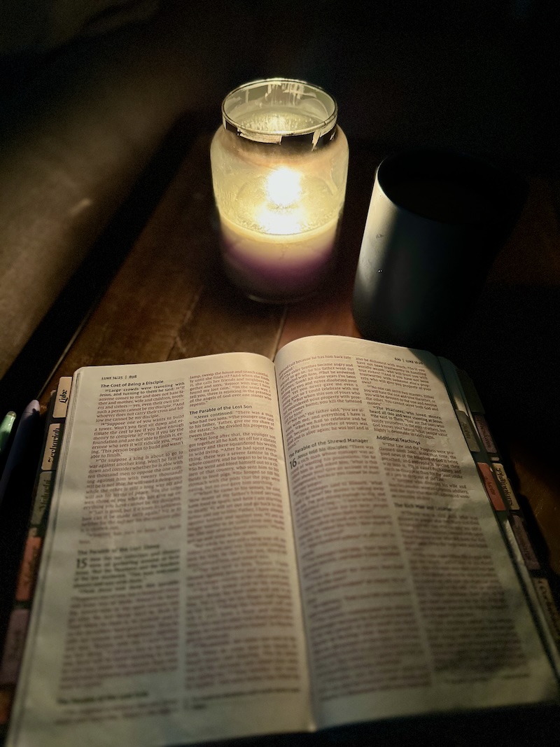 Bible, candle and coffee sitting on coffee table in dark