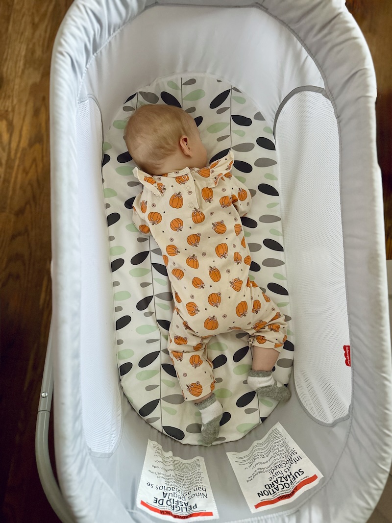 Baby girl wearing a pumpkin outfit sleeping in bassinet