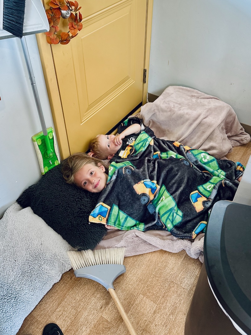 Brother and sister snuggling under blankets on floor