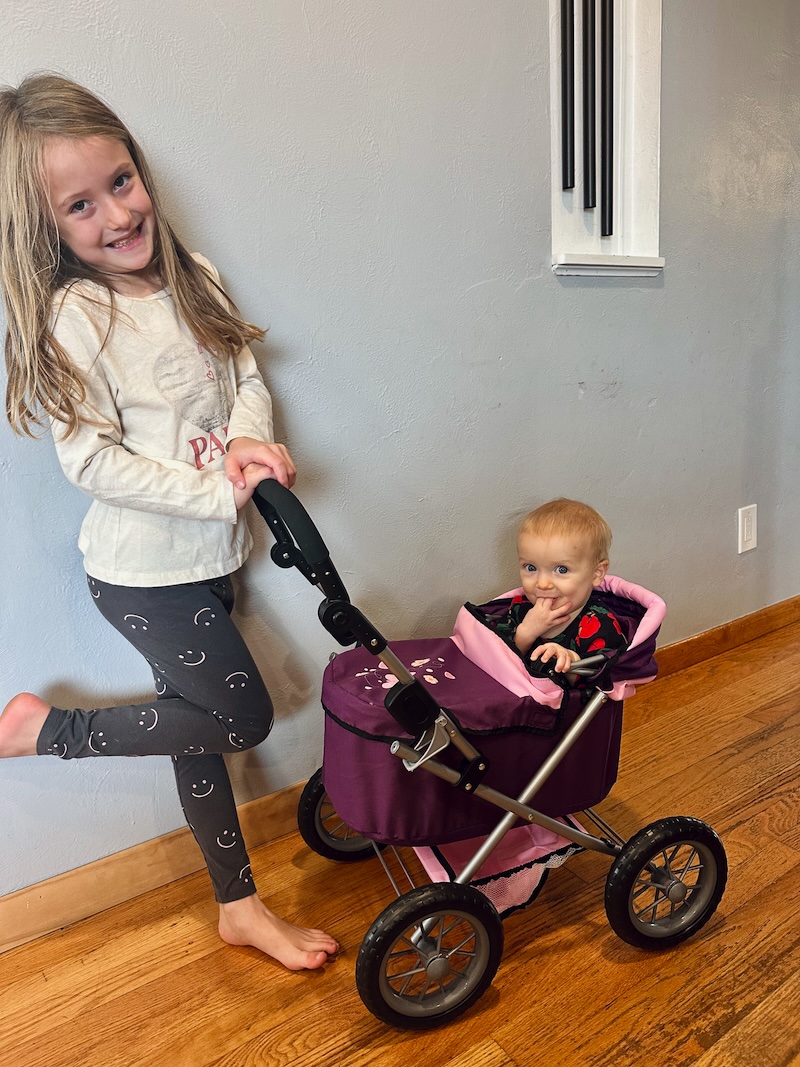 Girl pushing baby sister in toy stroller