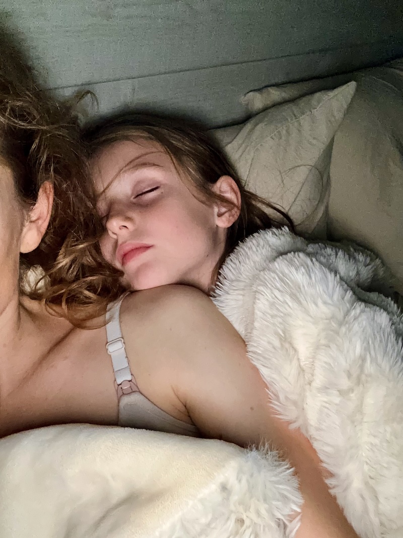 Girl sleeping on mom's shoulder in bed