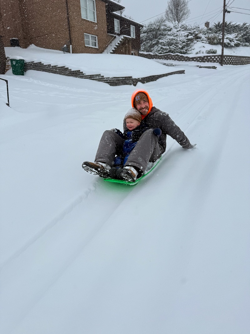 Dad and son sled riding down street