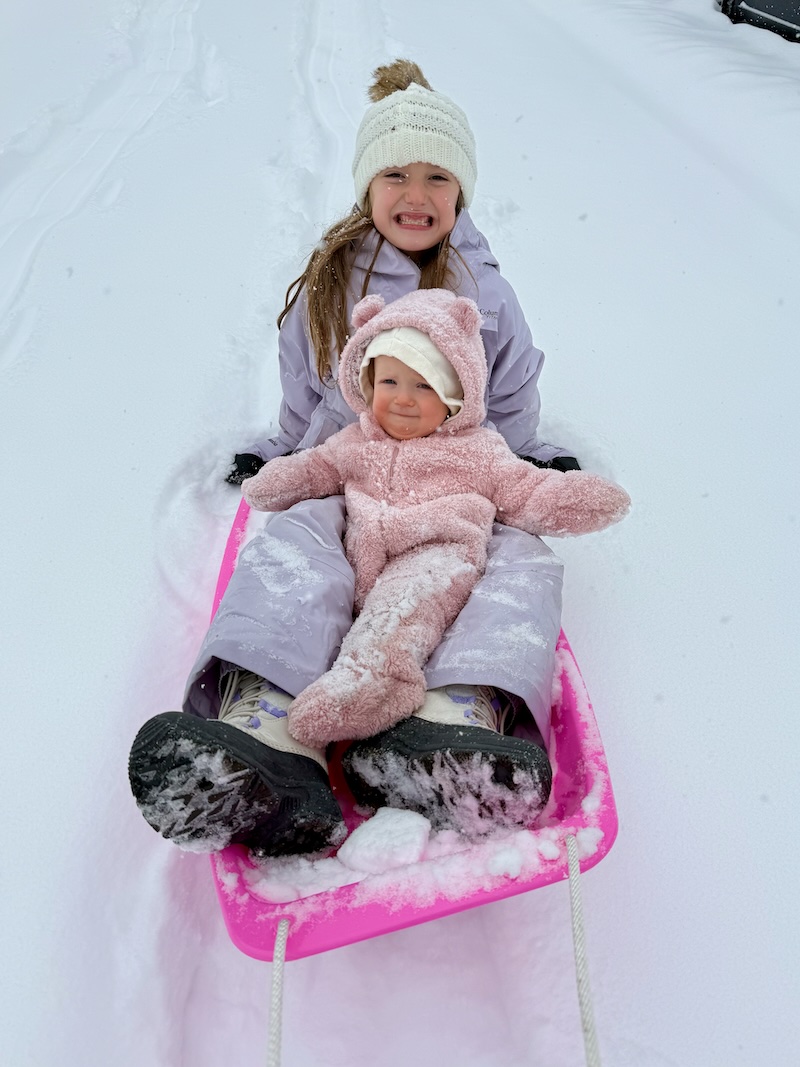 Girl and baby sitting on sled in snow
