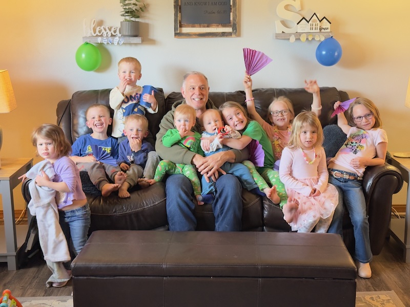 Grandpa sitting with ten grandkids on couch