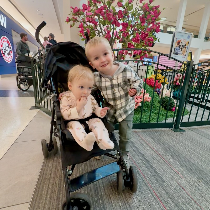 Toddler and baby in front of Easter display inside a mall