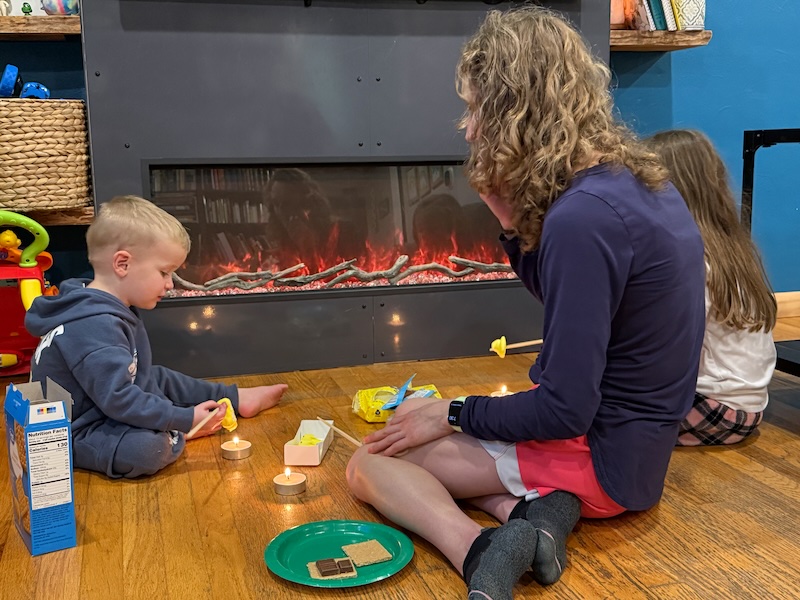 Mom and kids sitting on floor making indoor s'mores with Peeps and tea light candles