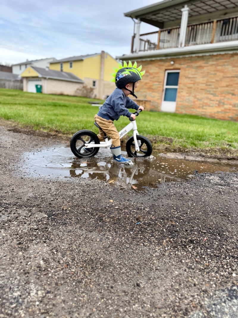 Toddler boy riding bike through puddle