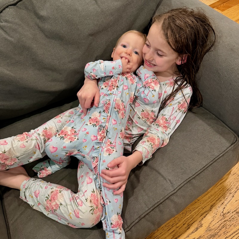 Baby and big sister with matching Eiffel Tower pajamas sitting on couch