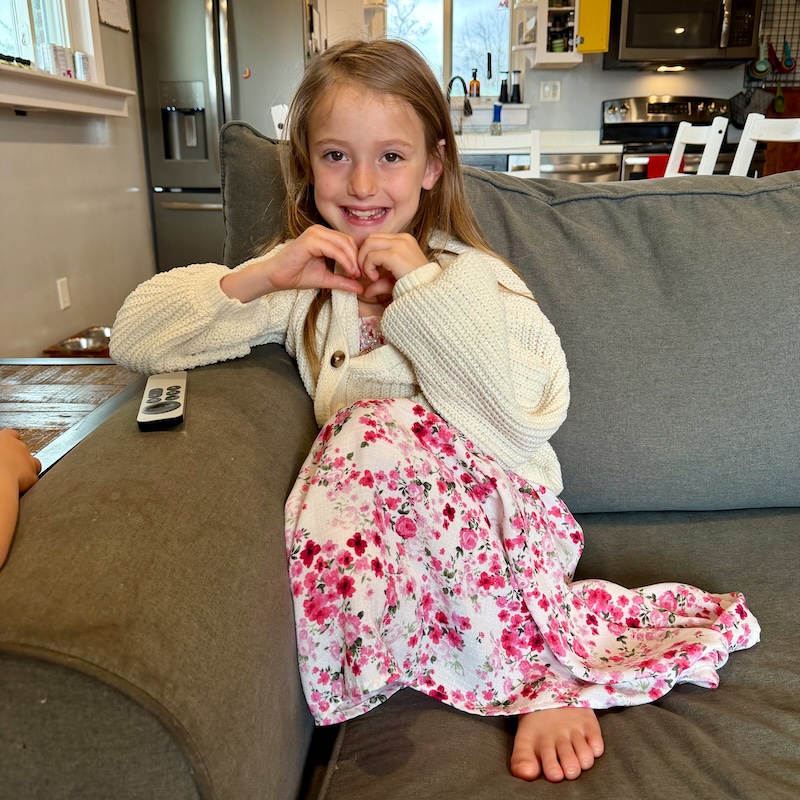 Girl sitting on couch making heart with her hands