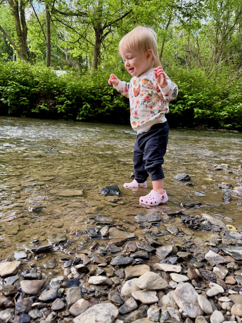 Baby girl standing in water at creek