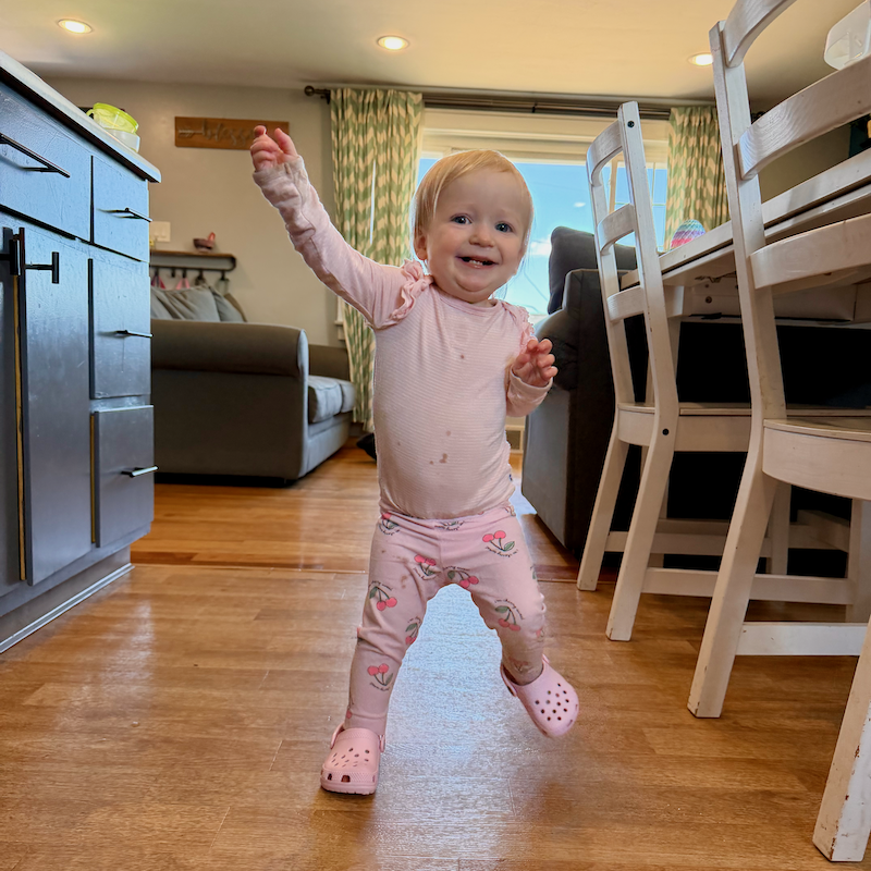 Baby girl walking in kitchen while wearing pink outfit and Crocs shoes