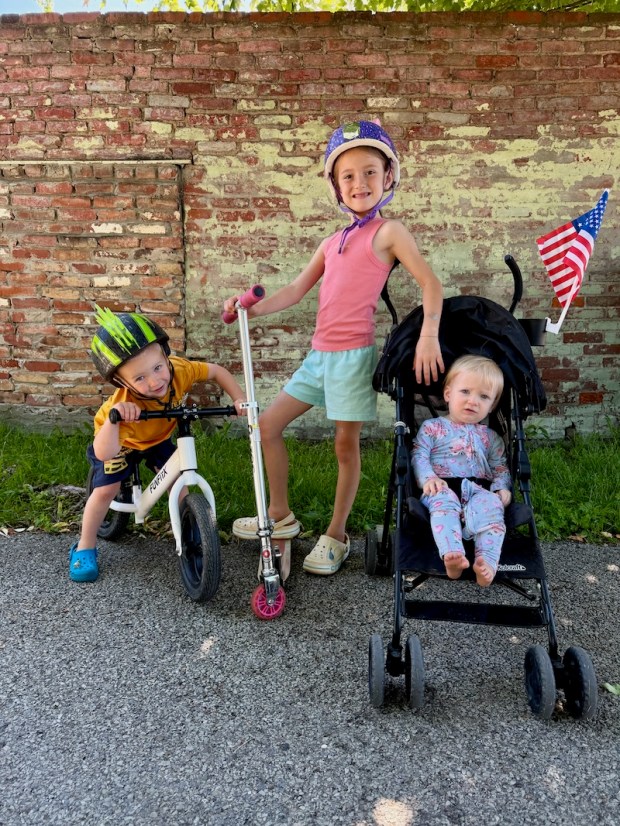 Kids standing against a wall with stroller, bike, and scooter