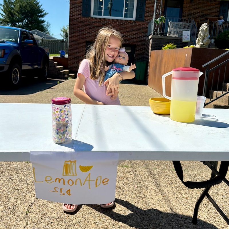 Girl holding baby doll at lemonade stand