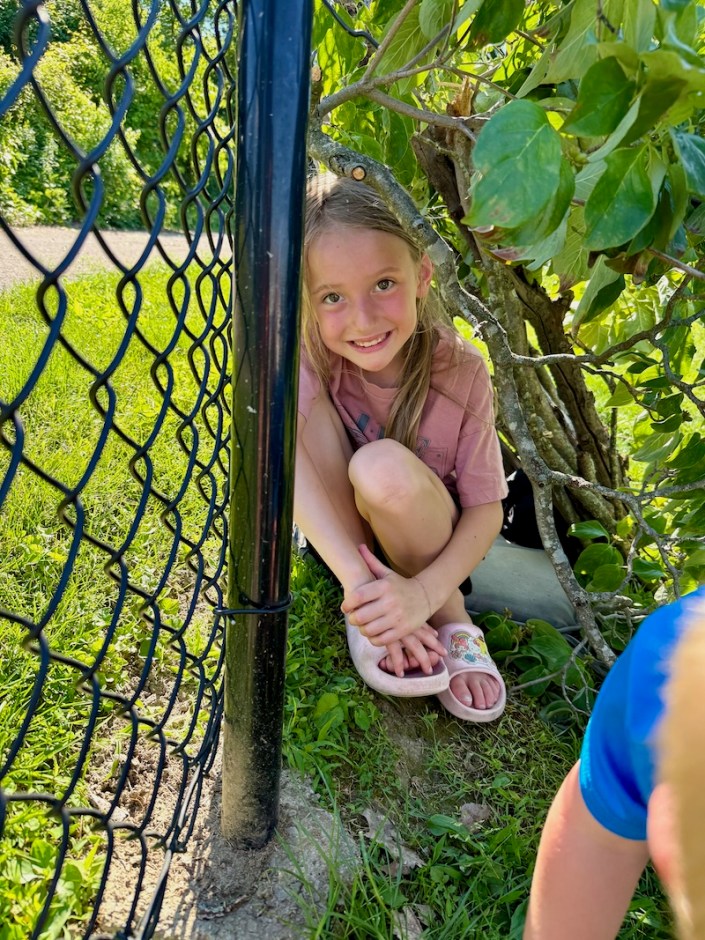Girl sitting in lean-to shelter against fence