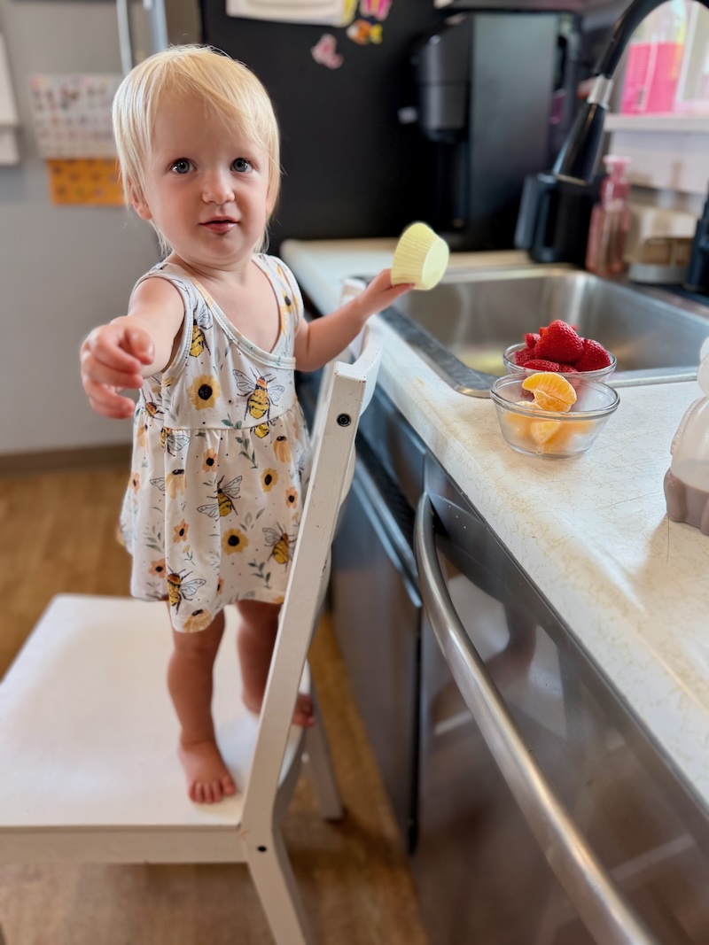 Toddler girl with muffin cup standing on kitchen chair