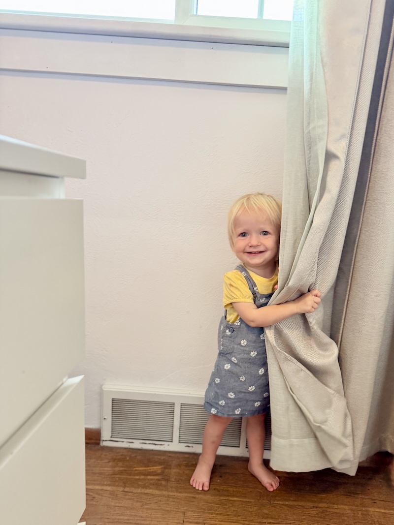 Toddler girl standing by curtains playing peek-a-boo