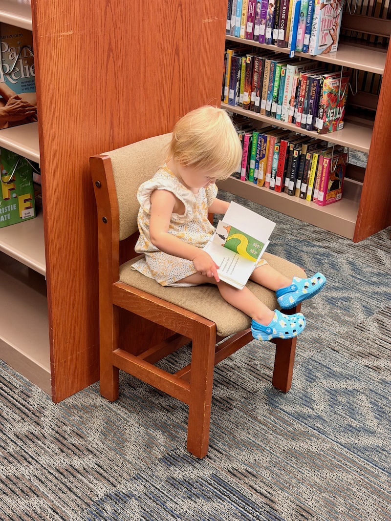 Toddler girl reading book at library