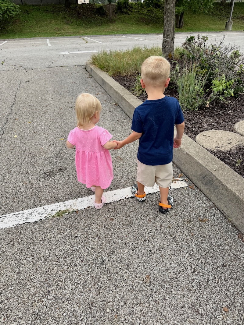 Toddler boy and girl holding hands while walking in a parking lot