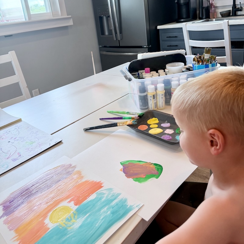 Toddler boy painting at kitchen table