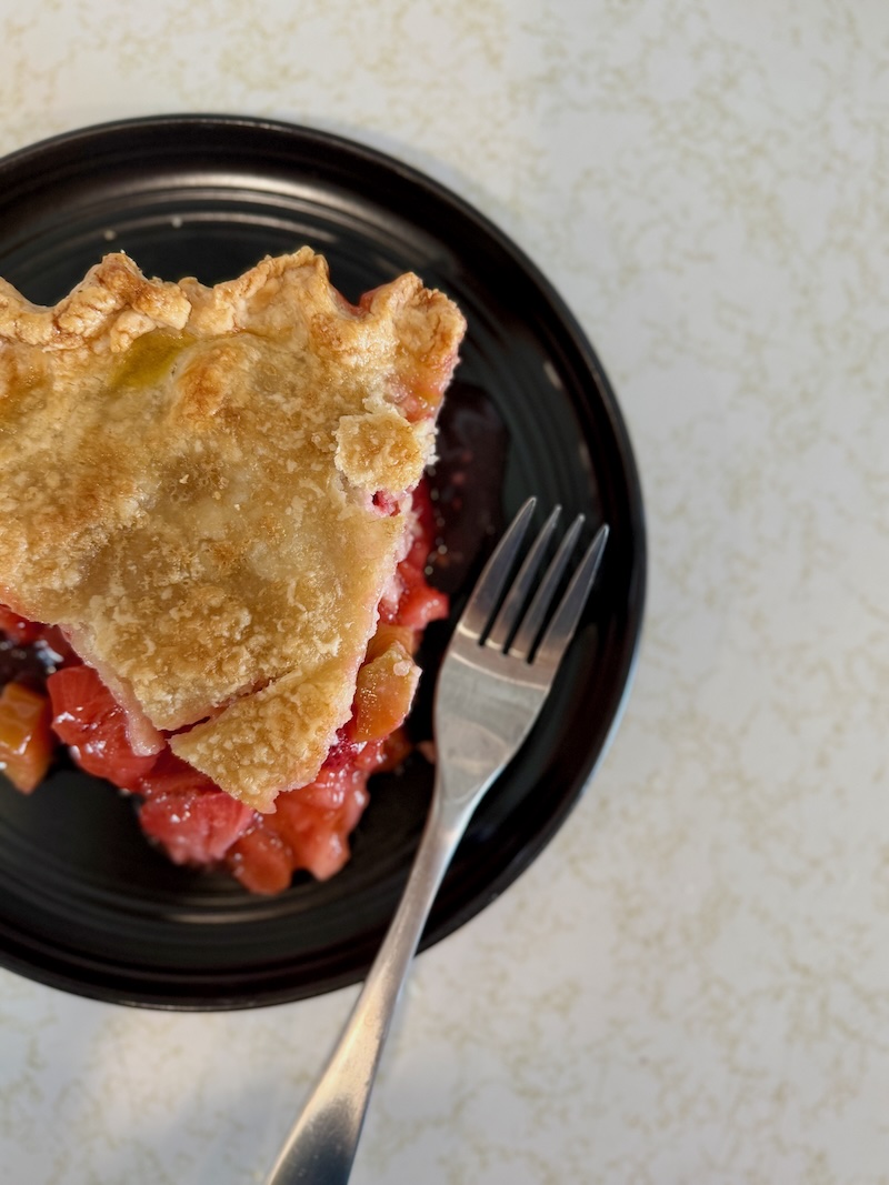 Slice of strawberry rhubarb pie on a black plate