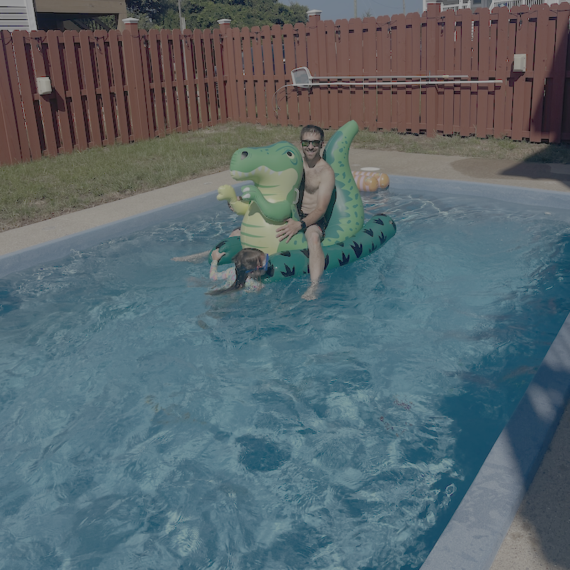Dad and daughter on dinosaur float in pool