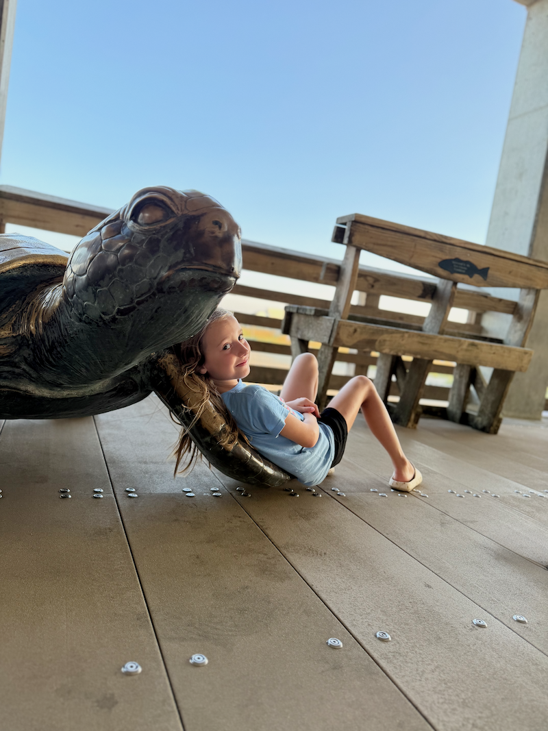 Girl leaning against turtle statue at Jennette's Pier in Nags Head, NC